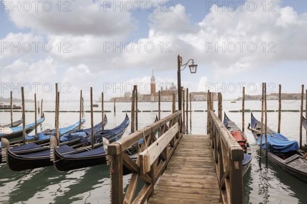Scenic view of a wooden dock leading to gondolas in Venice, Italy. The background showcases the