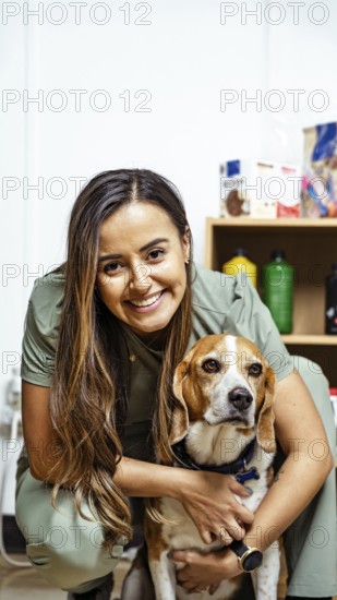 A nutritionist smiles warmly, embracing a beagle in an office setting. Shelves with nutritional