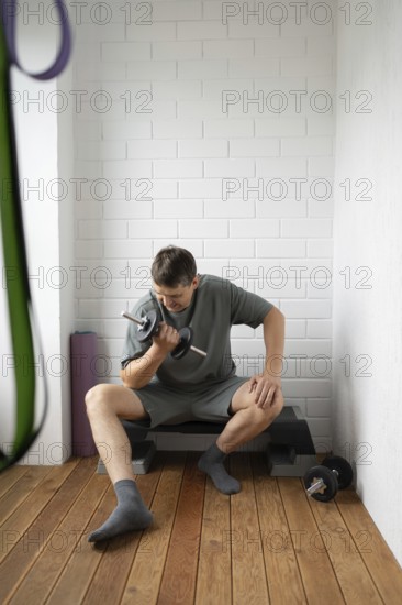 A man in comfortable clothing is seated on a step bench, focused on exercising with a dumbbell in a