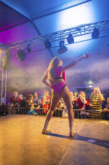 A dancer performs on a colourful stage in front of a celebrating audience, carnival, Schlagerkuchen