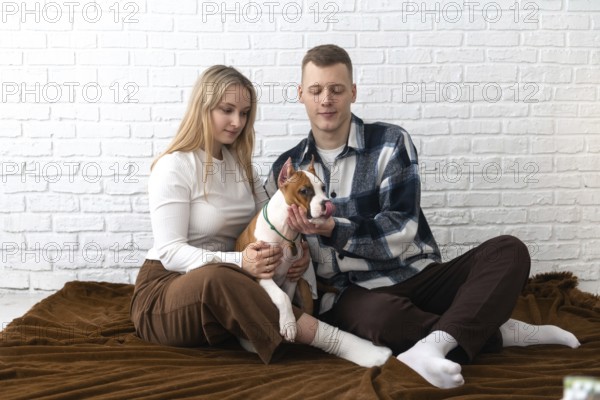 A young couple enjoys a peaceful moment with their Staffordshire Terrier puppy dog inside their