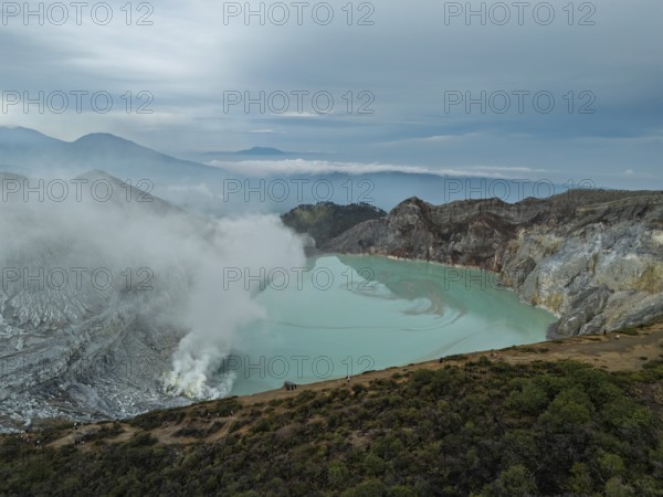 Drone view of Ijen crater in Indonesia with turquoise acidic lake and visible sulfur smoke near the