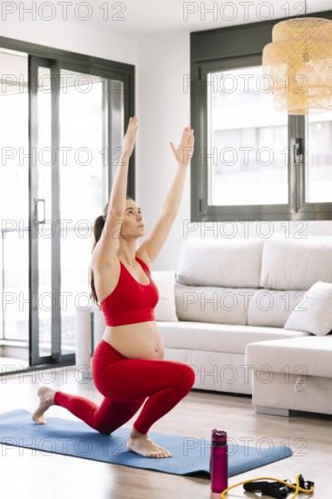 A pregnant woman practices yoga on a mat in a cozy living room, focusing on wellness and relaxation