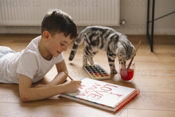 A boy lies on the floor, drawing a Mother's Day card with vibrant paints. His dedicated expression
