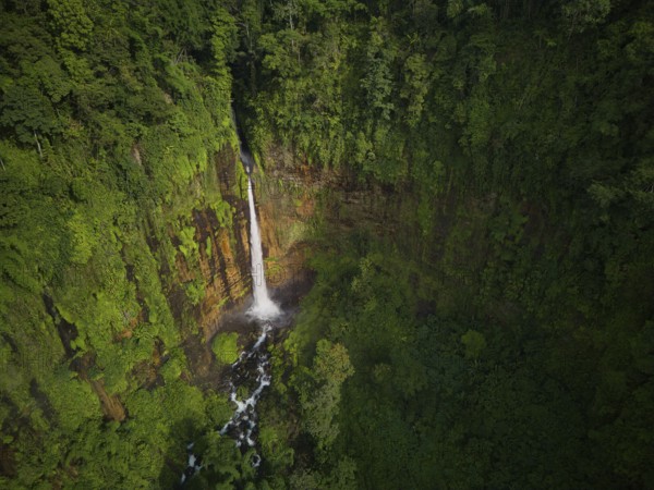 Aerial shot capturing the majestic Kaspa Biru Waterfall descending into a natural gorge, surrounded