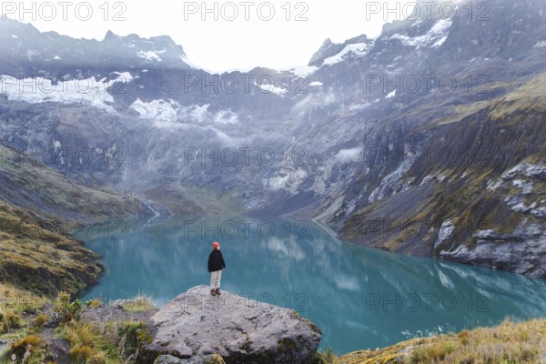 A woman stands on a rocky ledge, overlooking the stunning turquoise lake and surrounding peaks of