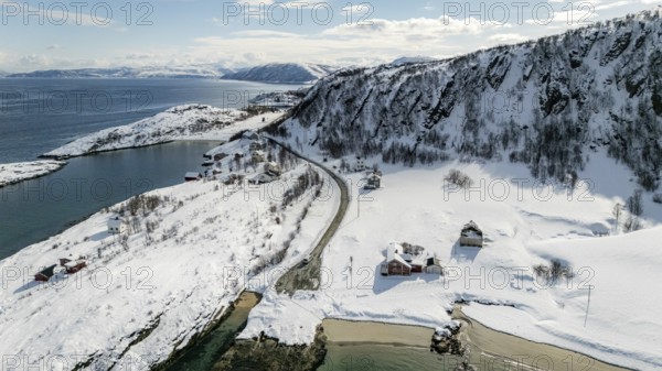 Aerial view of a serene Nordic landscape showcasing a snow-covered coastline, winding road, and