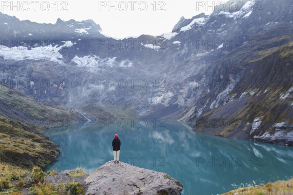 An Ecuadorian woman stands on a rocky ledge, overlooking the serene turquoise waters and majestic