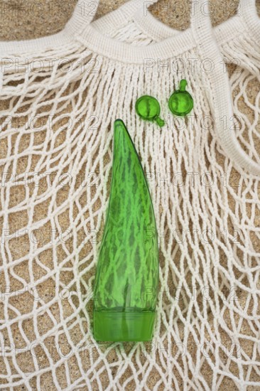 Top view of a green aloe vera gel tube and two green capsules placed on a white net bag, set