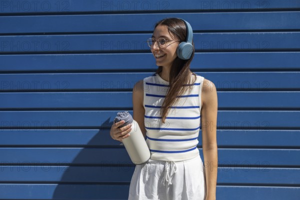 Smiling woman enjoying her active outdoor lifestyle in the city, wearing headphones and holding a
