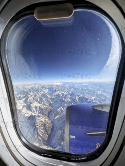 Stunning aerial view of a vast snow-covered mountain range as seen through an airplane window. The