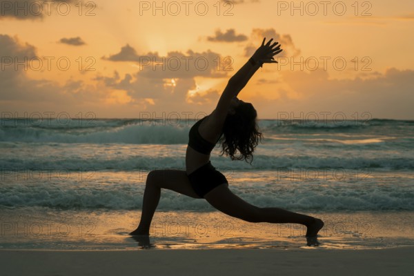 A woman practices yoga on a beach at sunrise, striking a graceful pose that symbolizes balance,