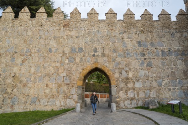 An Asian woman walks through an arched entrance of a medieval city wall in Avila, Spain, surrounded