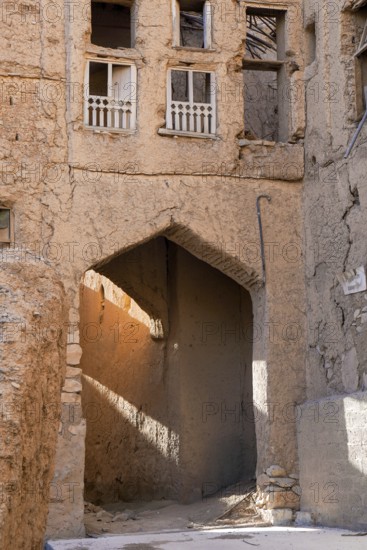 A textured, sunlit archway casts golden hues across the crumbling facades of traditional mud-brick