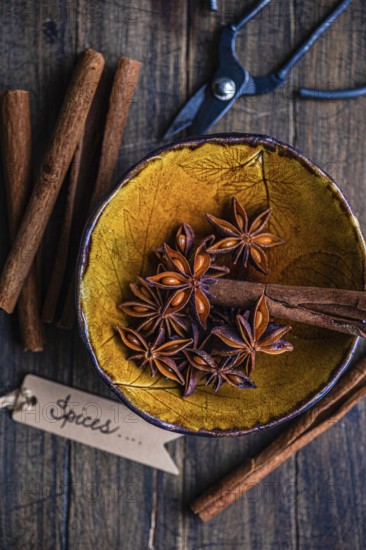 Top view of a rustic yellow bowl filled with star anise and cinnamon sticks, accompanied by a pair