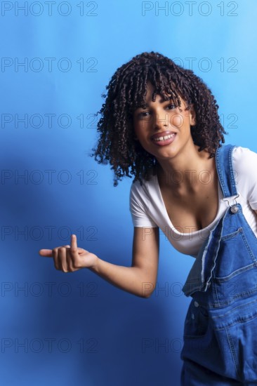 Young woman with curly hair pointing her finger to the left side of the frame while smiling on a