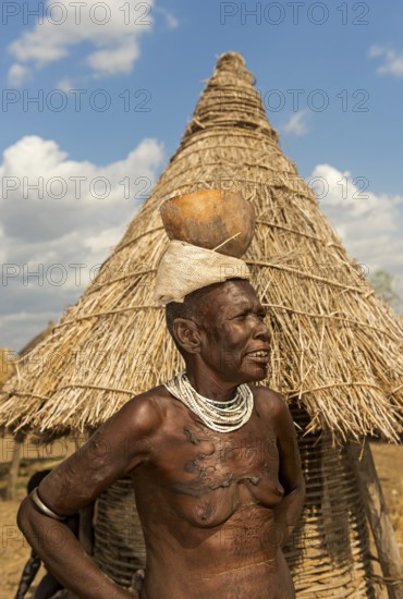 Woman with scar tattoo on her upper body carrying a calabash drinking bowl on her head, ethnic