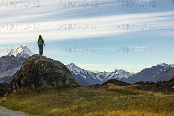 A woman stands on a rocky outcrop overlooking Mount Cook in New Zealand, surrounded by stunning