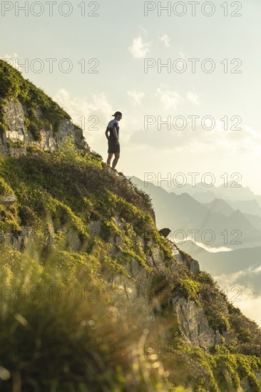 A lone man stands on a scenic mountain trail, taking a moment to rest during an invigorating run.