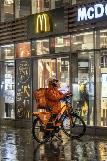 Street at the main station, Lieferando courier, cyclist, rainy weather, city centre, in the