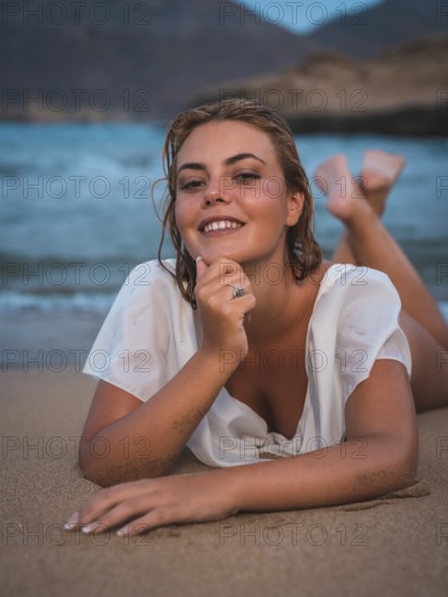 Lifestyle of a blonde Caucasian girl in a white swimsuit. Smiling in the sand after getting out of