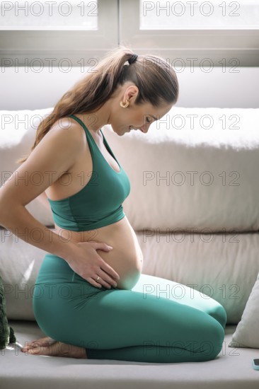 A pregnant woman wearing a green yoga outfit is practicing wellness and mindfulness in a serene