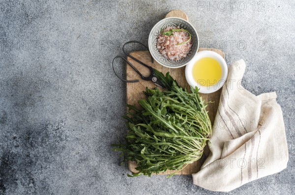 Fresh arugula, Himalayan pink salt, and olive oil arranged on a rustic wooden cutting board with