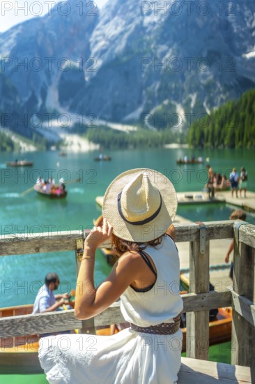 Tourist wearing summer hat looking at lake braies, also called pragser wildsee, with boats and