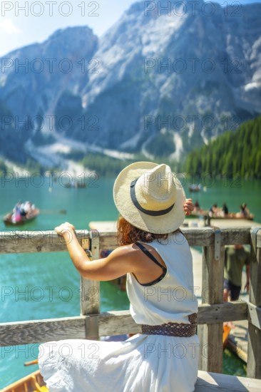 Woman wearing straw hat admiring scenic landscape of lake braies with boats and turquoise water in