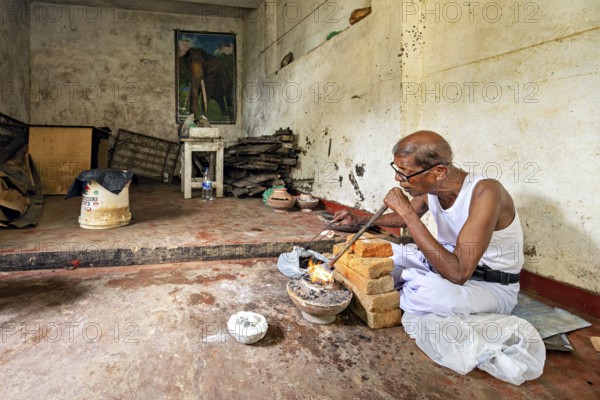 An old man works silently in a workshop with bricks and fire, an elephant poster on the wall, a man