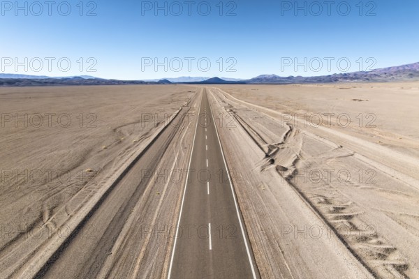A straight road stretches across a vast desert landscape of the argentine Puna, leading into