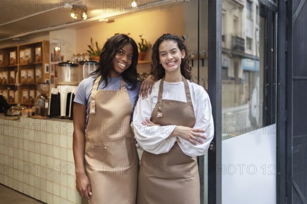 Two friendly clerks stand proudly at the entrance of an organic bulk store, wearing aprons and