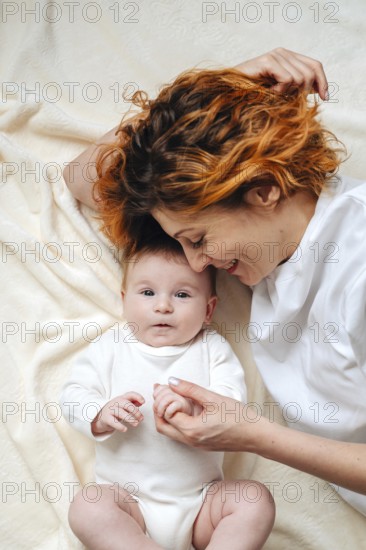 A mother shares a tender moment with her newborn baby girl, lying on a soft, cream-colored blanket.