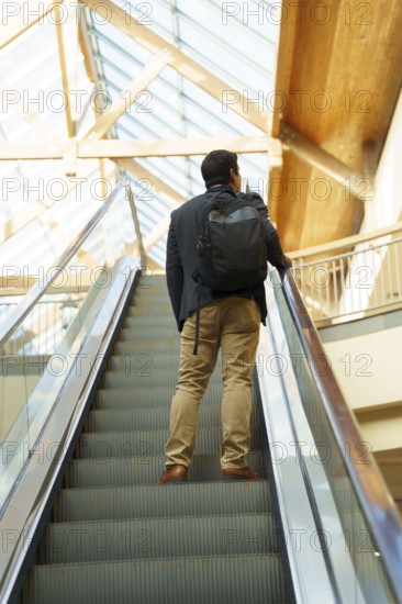 Young Chilean businessman in smart attire with a backpack ascends an escalator in a modern,