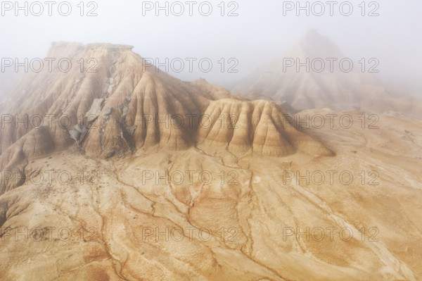 Aerial view of rugged desert formations enveloped in mist Erosion patterns are visible on the sandy