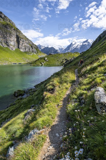 Mountaineer on a hiking trail at a mountain lake with a view of glaciated mountain peaks, Lac du