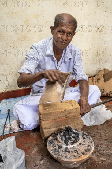 Elderly man works with bricks and coal in traditional clothes, a man burns sapphires in a small
