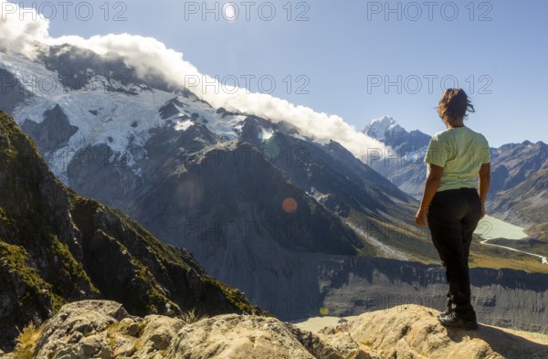 A woman enjoys the stunning autumn view of Mount Cook, New Zealand, standing on a rocky vantage