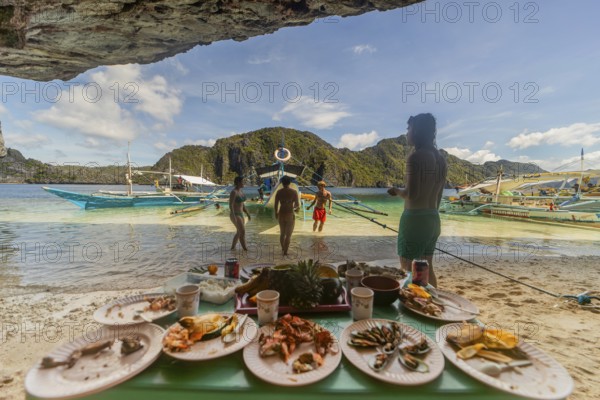 Unrecognizable tourists enjoy a seaside meal in the Philippines, showcasing a vibrant beach