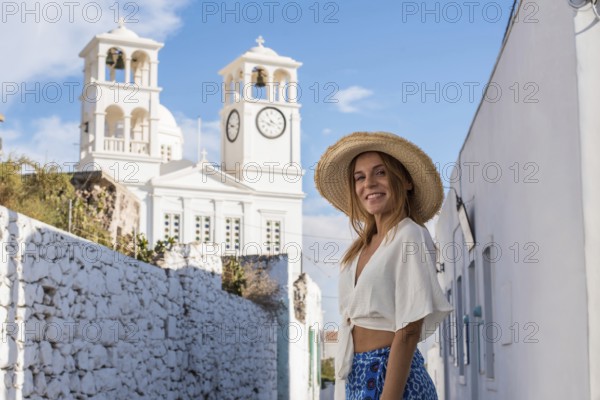 A smiling woman in a straw hat enjoys a sunny day exploring the charming village of Trypiti, Milos