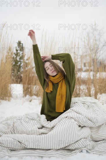 A woman with a serene expression stretches in a snowy park, wearing a green sweater and yellow