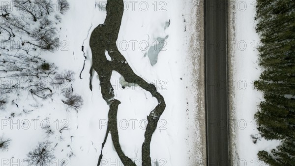 Aerial view of a Nordic landscape showcasing a road flanked by a frozen stream and snow-laden trees