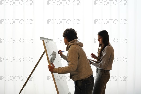 Two teenagers, a non-binary individual and a female, participate in an writing activity, o a