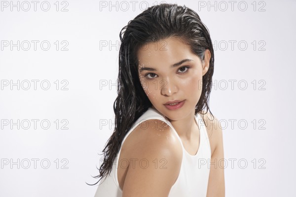 A striking female model with wet hair looks at the camera, showcasing a natural beauty look in a