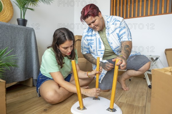 Lesbian friends assembles a small table in their new home, surrounded by boxes. They work together