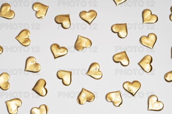 Numerous golden heart shapes artistically arranged on a plain white surface, symbolizing love and