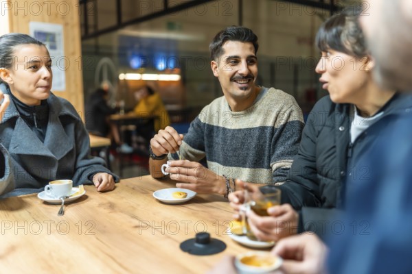 Diverse group of friends socializes and talks while drinking coffee and tea at a wooden table in an