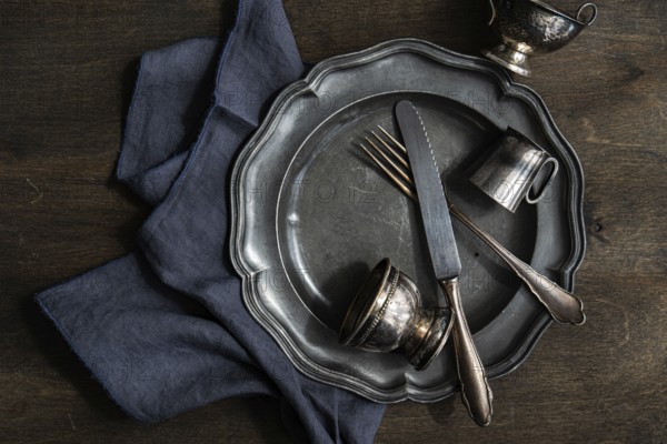 A collection of vintage silver plate, cutlery, and cups arranged on a dark wooden surface with a