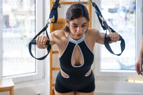 Woman using suspension straps for trx style physiotherapy, focusing on strength and rehabilitation