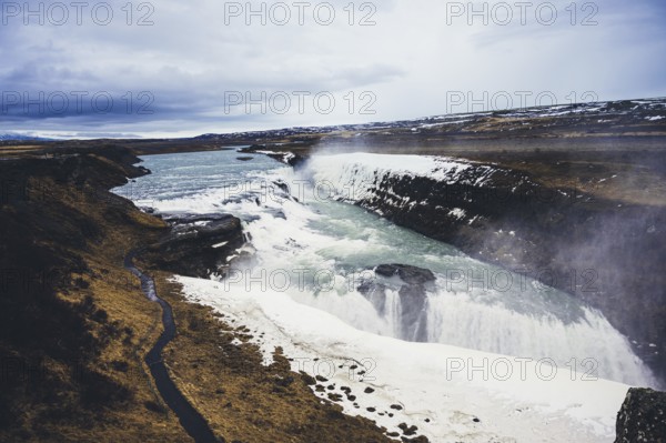 Stunning view of Gullfoss waterfall, cascading powerfully over rugged cliffs. The icy landscape and